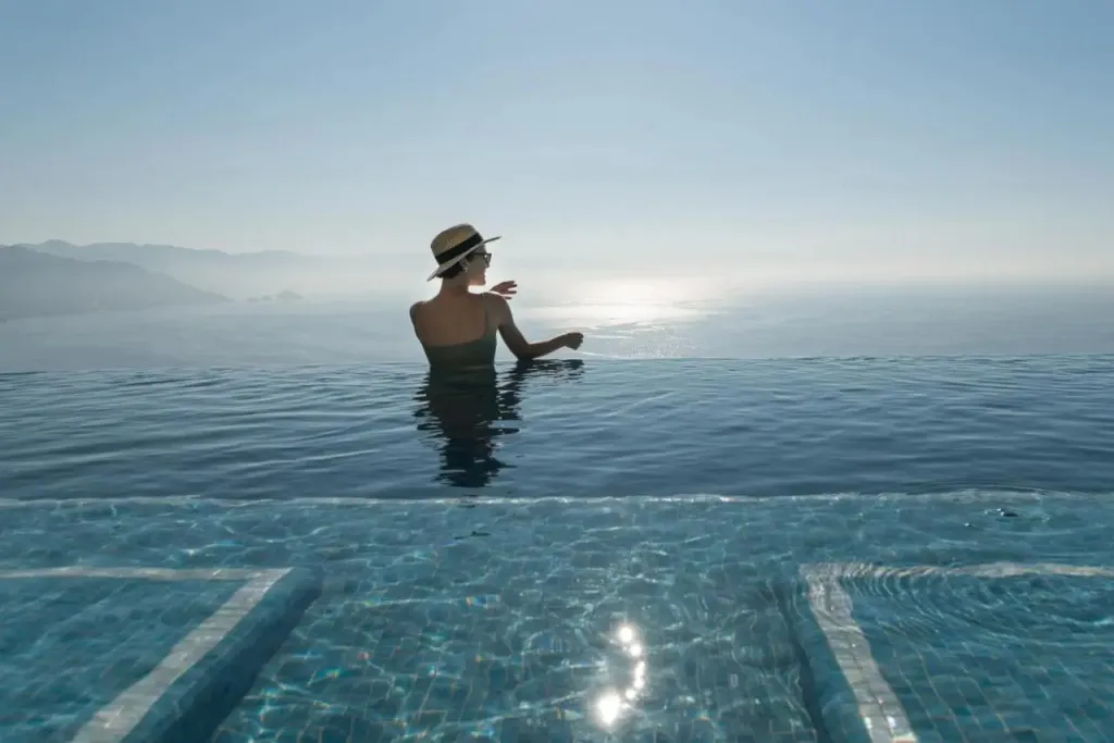 Une personne se tient dans l'eau d'une piscine à débordement face à la mer.