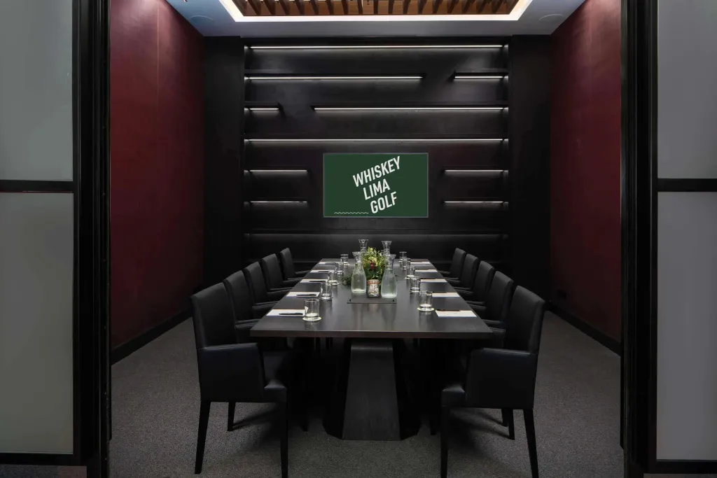 Une longue table de réunion est entourée de chaises dans une salle aux murs sombres.