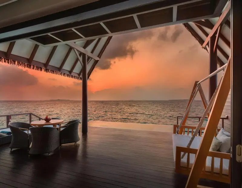 Terrasse en bois avec mobilier d'extérieur donnant sur une mer calme au coucher du soleil.