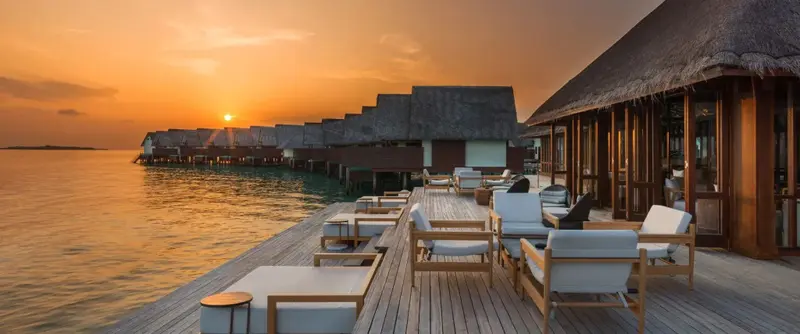 Terrasse en bois avec mobilier d'extérieur face à l'océan au coucher du soleil.