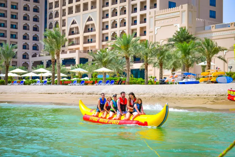 Des vacanciers profitent d'une balade en bouée jaune sur une mer turquoise face à un hôtel.