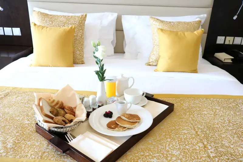 Un plateau de petit-déjeuner est servi sur un lit bien fait avec des oreillers décoratifs.