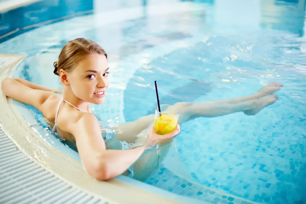 Une jeune femme se détend dans une piscine avec un cocktail.
