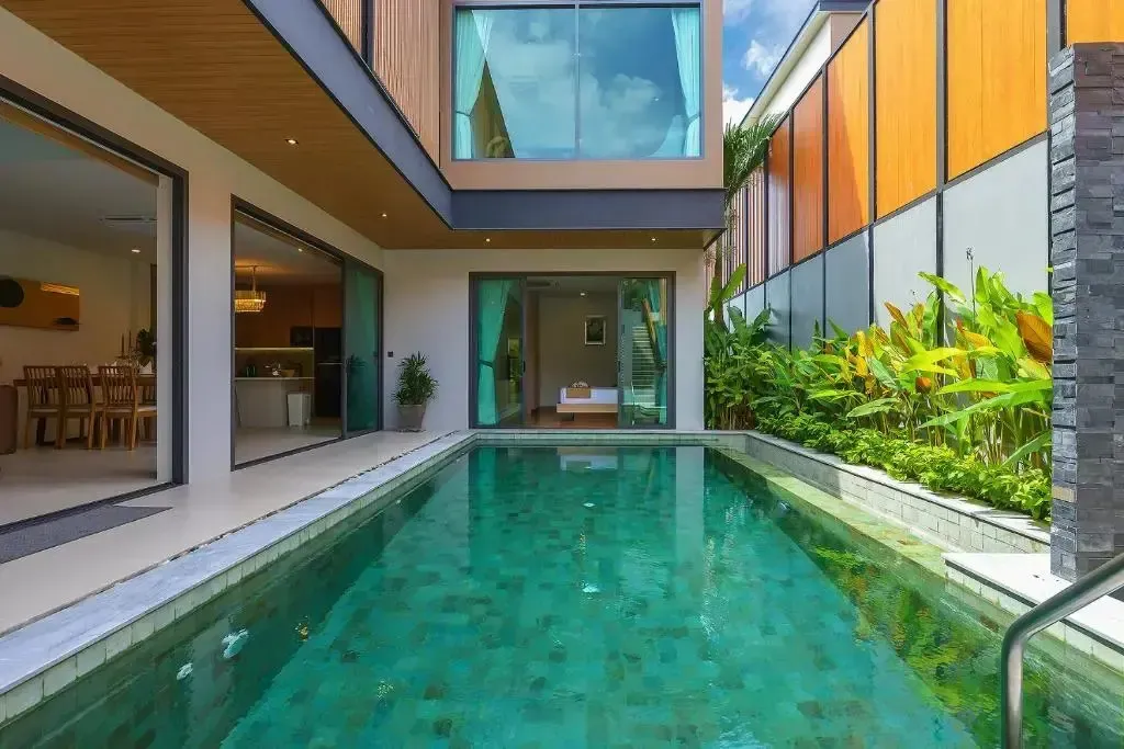 Une piscine rectangulaire turquoise est entourée d'une terrasse et de végétation luxuriante.