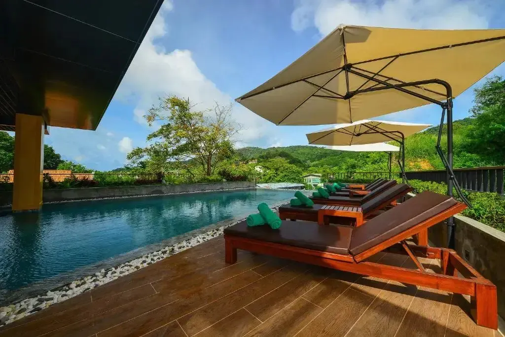 Transats et parasols ombragent une terrasse au bord d'une piscine turquoise.