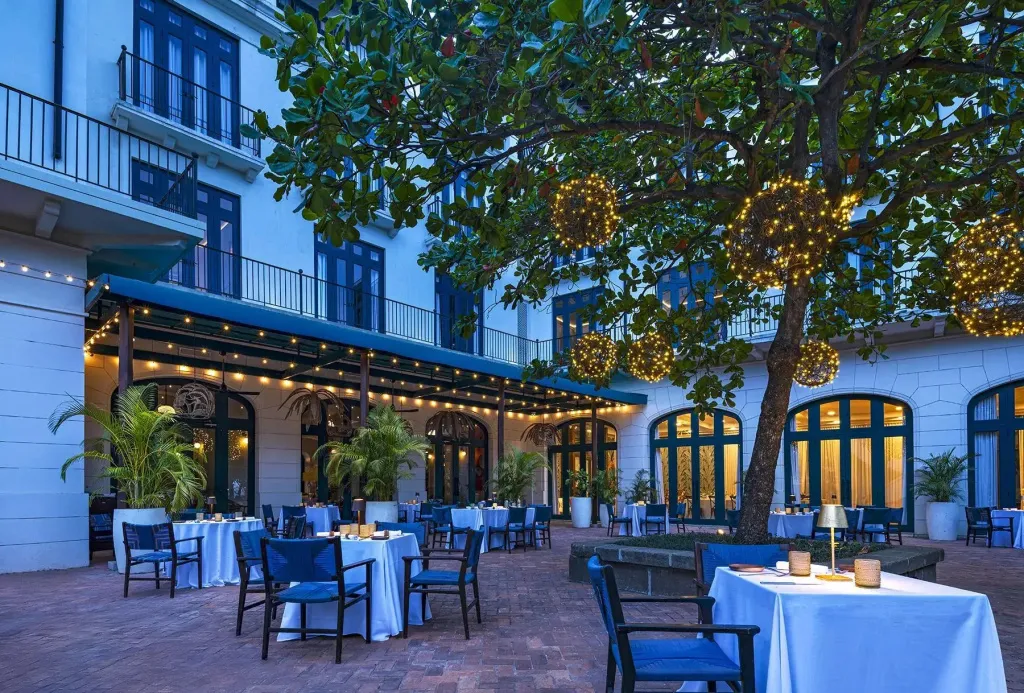 Une terrasse pavée avec des tables dressées pour un repas en extérieur, éclairée par des guirlandes lumineuses.