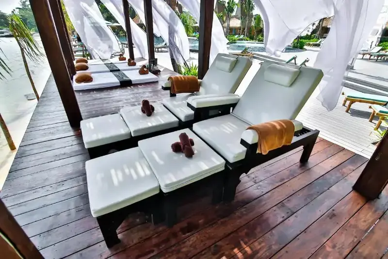 Transats blancs et bruns disposés sur une terrasse en bois ombragée.