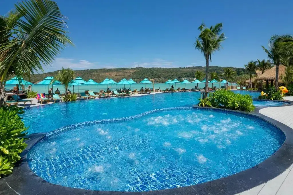 Une piscine turquoise avec des transats et des parasols le long d'une plage.