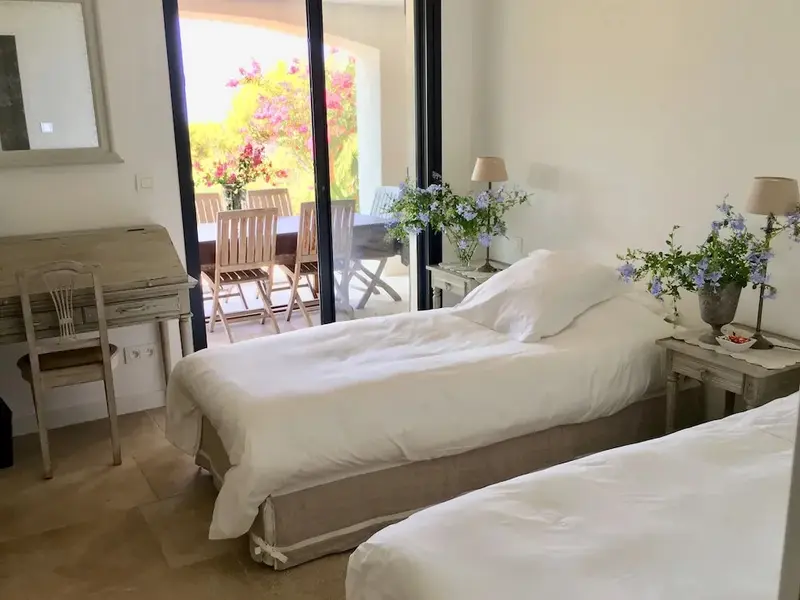 Une chambre lumineuse avec deux lits simples donnant sur une terrasse fleurie.