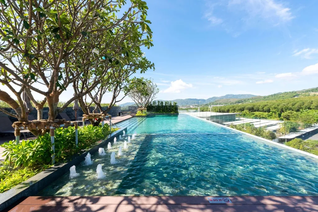 Une piscine rectangulaire avec des jets d'eau, entourée d'une végétation luxuriante et d'une terrasse.