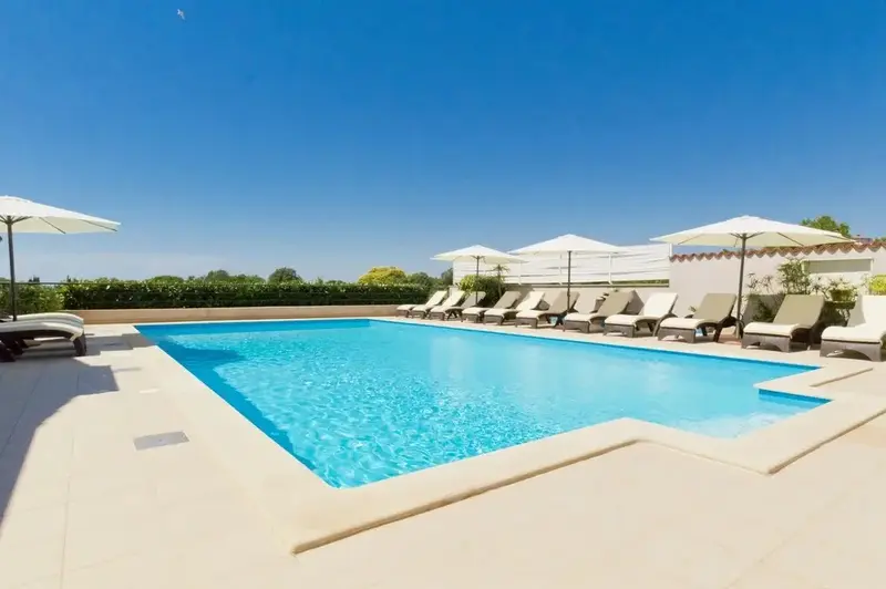 Une piscine rectangulaire bordée de transats sous des parasols blancs.