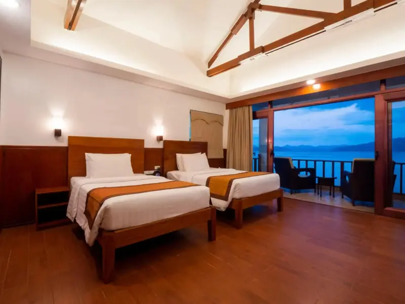 Chambre lumineuse avec deux lits simples donnant sur une vue mer.