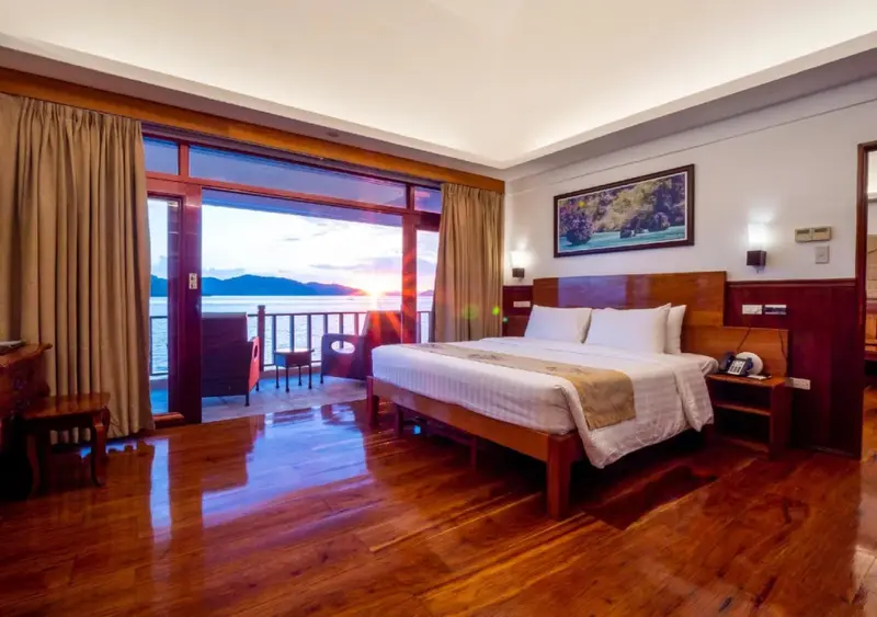 Une chambre spacieuse avec un grand lit donnant sur une vue mer au lever du soleil.