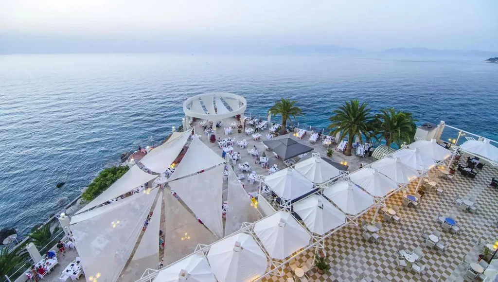 Terrasse ombragée avec tables et parasols surplombant la mer.