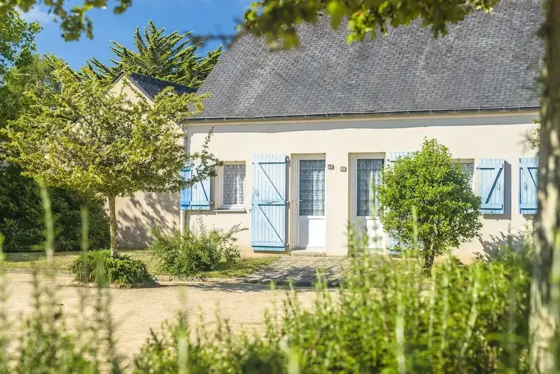 Façade d'un bâtiment clair avec des volets bleus et un jardin soigné.