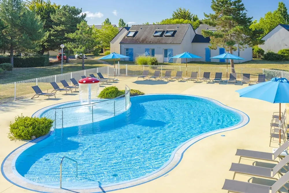 Une piscine ensoleillée avec des transats bleus et un bâtiment en arrière-plan.