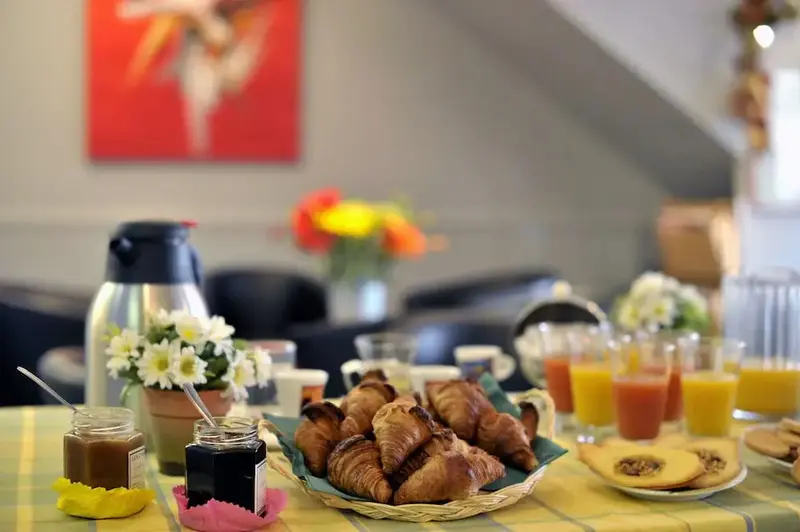 Une table est dressée avec des viennoiseries, des confitures et des jus de fruits.