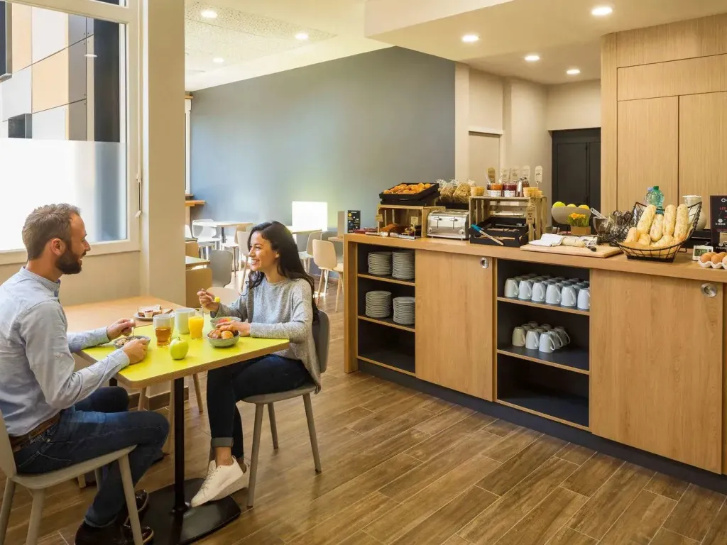 Un couple prend son petit-déjeuner à une table dans une salle lumineuse.