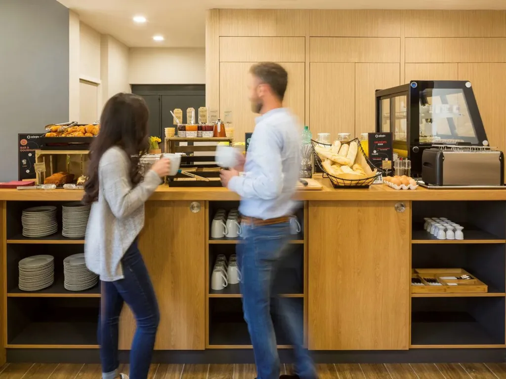 Des personnes se servent des viennoiseries et des boissons au comptoir d'un buffet.