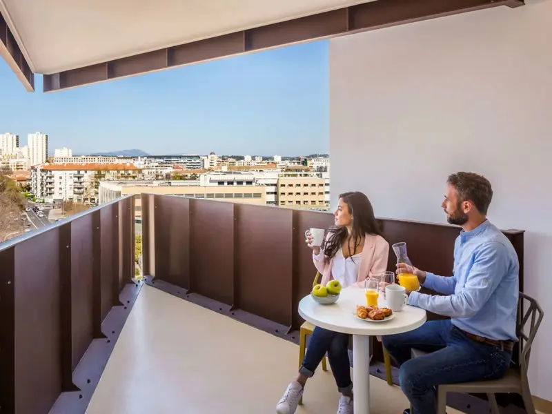 Un couple prend son petit-déjeuner sur un balcon avec vue sur la ville.