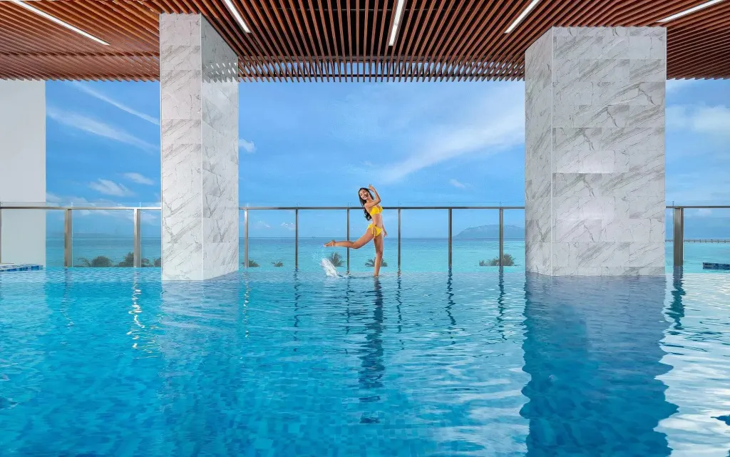 Une personne se tient dans une piscine à débordement avec vue sur la mer.