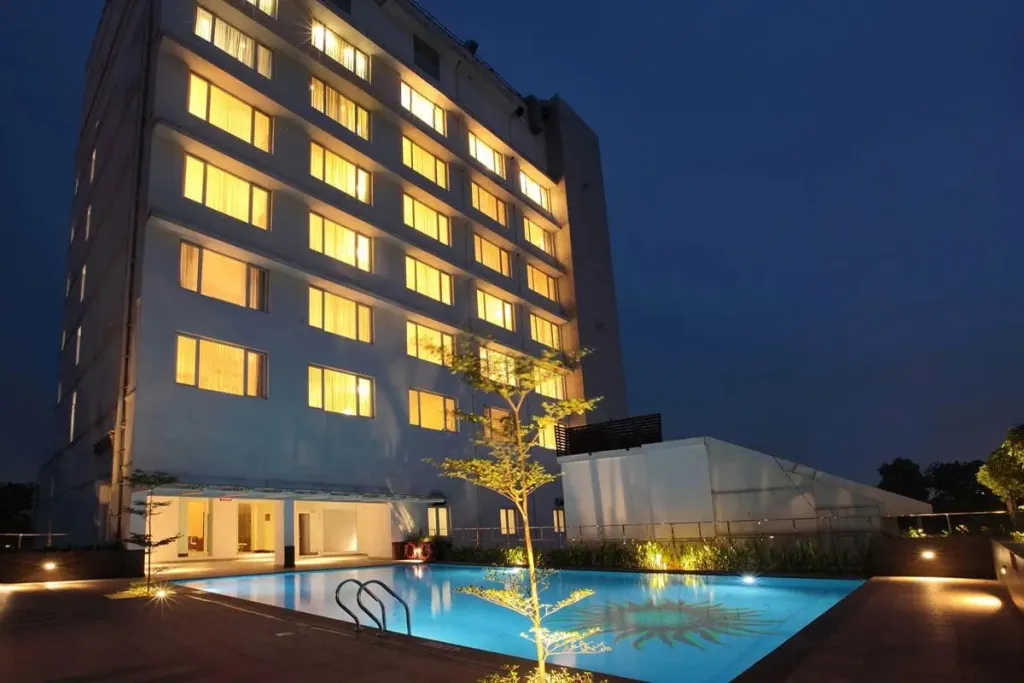 Bâtiment moderne illuminé avec une piscine au premier plan.