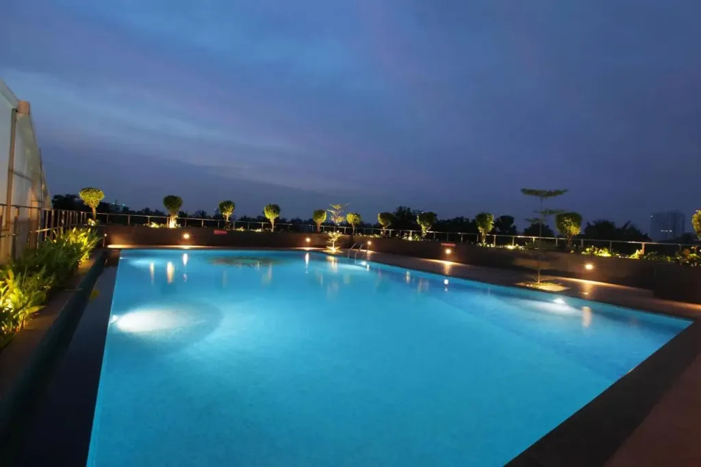 Piscine rectangulaire illuminée au crépuscule avec végétation soignée en arrière-plan.