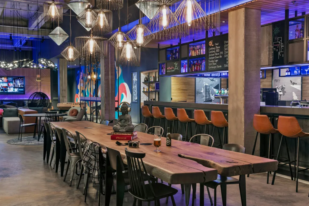 Une longue table en bois occupe le centre d'un espace lumineux avec un bar en fond.