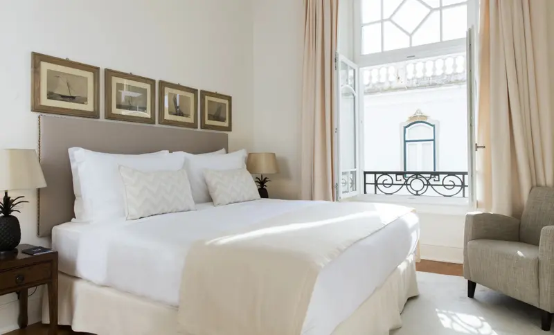 Une chambre lumineuse avec un grand lit et une fenêtre ouverte sur la ville.