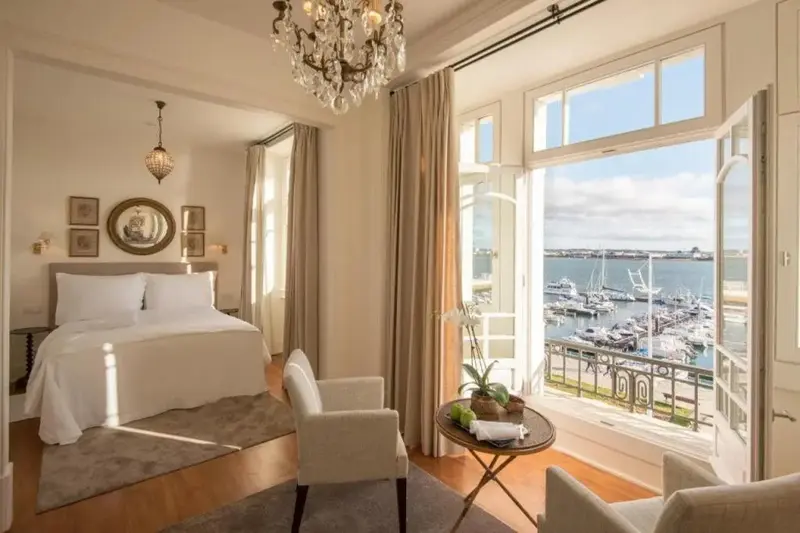 Chambre lumineuse avec un lit blanc et une vue sur un port de plaisance.