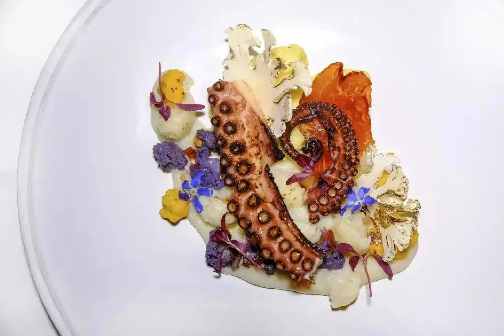 Assiette raffinée ornée d'un poulpe, de légumes et de fleurs comestibles.
