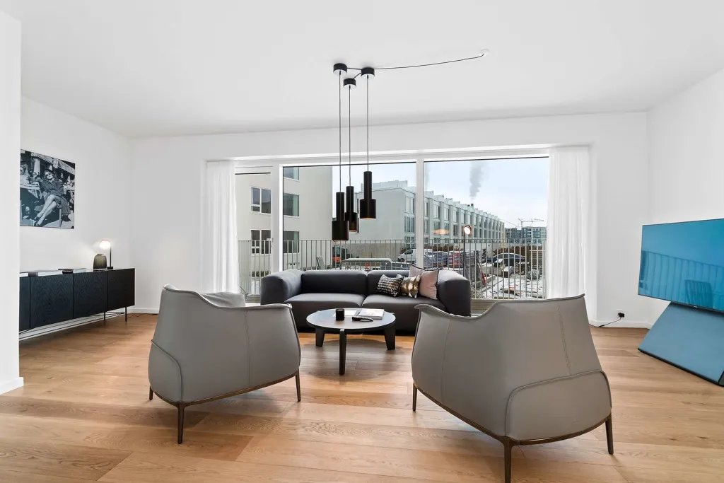 Un salon moderne avec canapés et fauteuils face à de grandes baies vitrées.