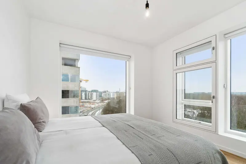 Une chambre lumineuse avec un lit fait et une vue sur la ville.
