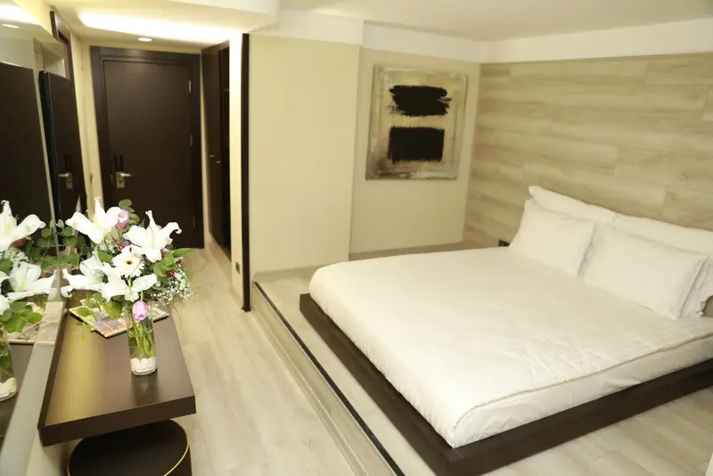 Une chambre lumineuse avec un grand lit recouvert d'une couette blanche et un bouquet de fleurs sur une table de chevet.