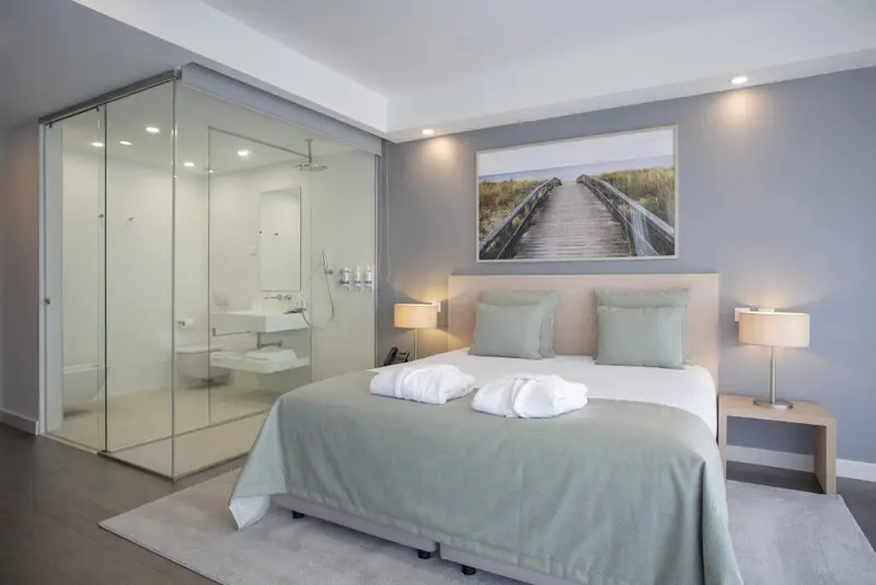 Une chambre lumineuse avec un grand lit et une douche à l'italienne en verre.