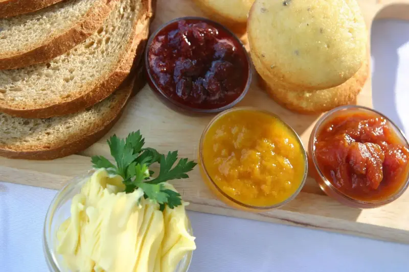 Assortiment de confitures, de pain et de beurre sur une planche en bois.