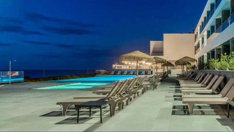 Une piscine illuminée au crépuscule avec des transats alignés sur une terrasse.