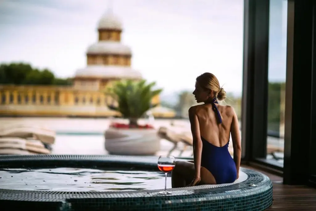 Une femme se détend dans un jacuzzi avec vue sur une piscine et un bâtiment.