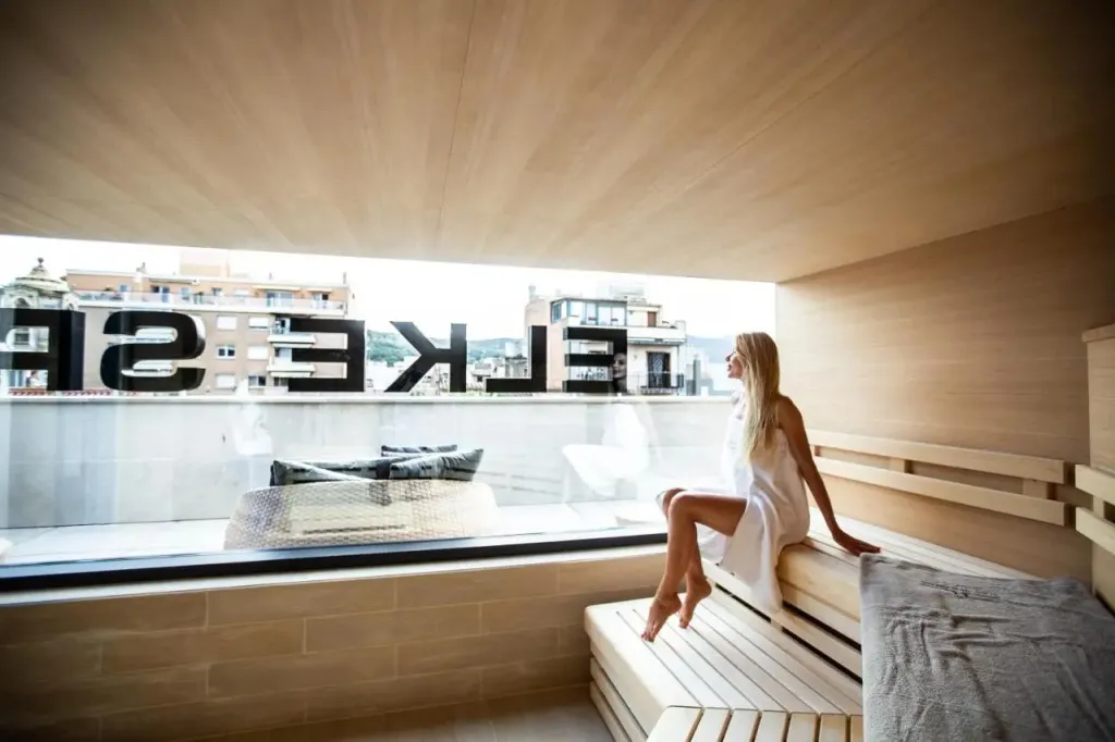 Une femme est assise sur une banquette en bois devant une grande fenêtre avec vue sur la mer.