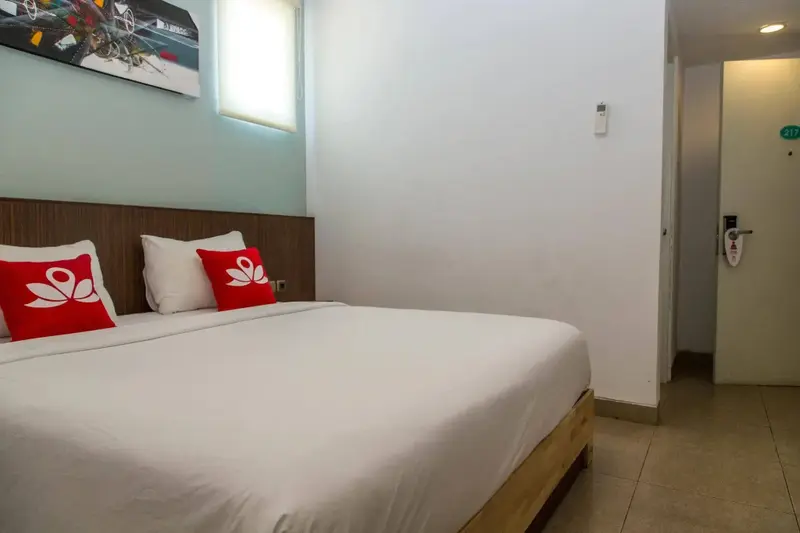 Une chambre lumineuse avec un grand lit recouvert de draps blancs et des oreillers rouges.