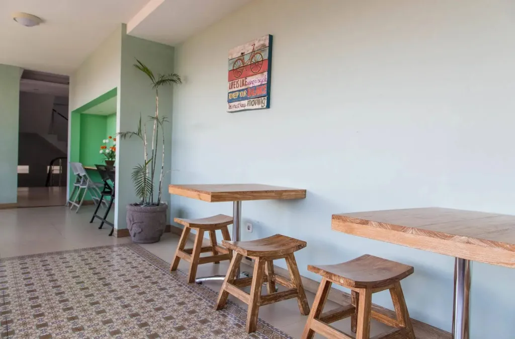 Tables et tabourets en bois adossés à un mur vert clair dans un espace intérieur.