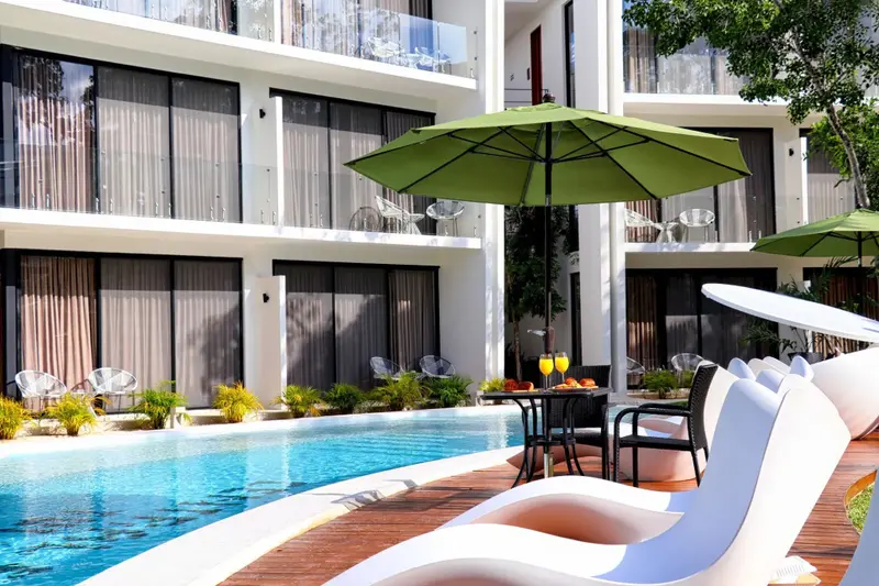 Transats blancs au bord d'une piscine turquoise avec un parasol vert.