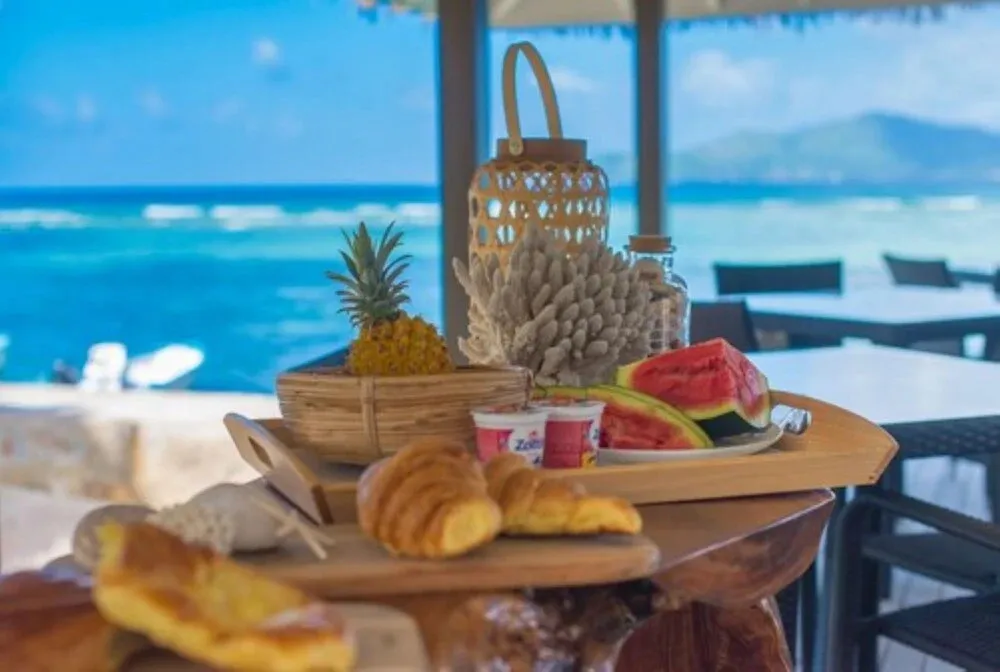 Une table basse présente un assortiment de fruits frais et de viennoiseries avec une vue sur l'océan.
