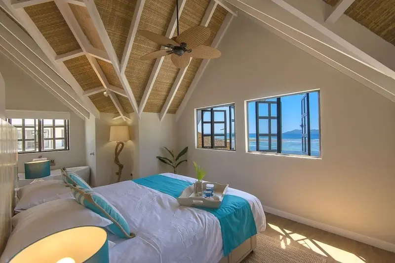 Une chambre lumineuse avec un lit turquoise face à une vue sur la mer.