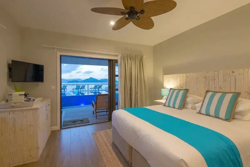 Une chambre lumineuse avec un grand lit donnant sur une terrasse et une vue sur la mer.