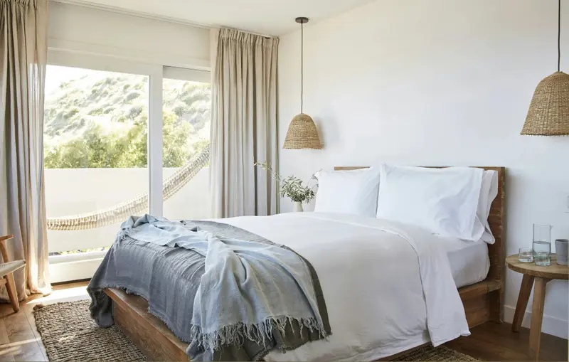 Une chambre lumineuse avec un grand lit recouvert d'une couverture bleue et donnant sur un paysage montagneux.