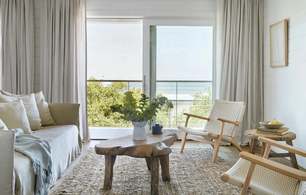 Espace de détente lumineux avec canapé et fauteuils en bois, donnant sur une vue mer.