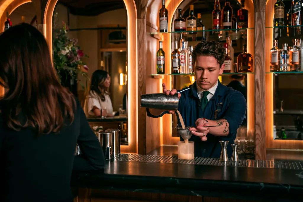 Un barman prépare un cocktail derrière un comptoir illuminé.