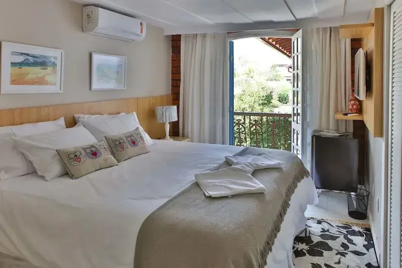 Une chambre lumineuse avec un grand lit et un balcon ouvert sur la végétation.
