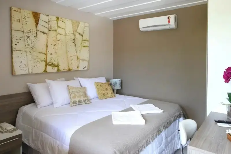 Une chambre lumineuse avec un grand lit recouvert d'une courtepointe blanche et de coussins.